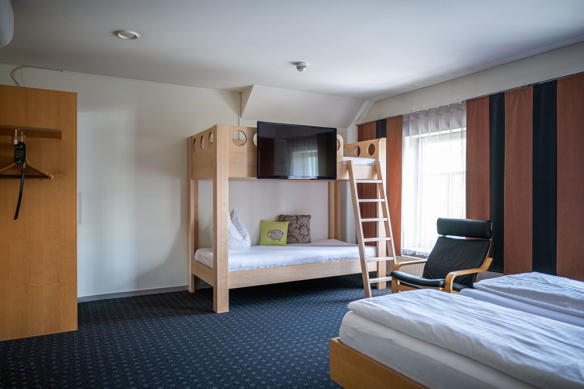 A bunk bed room with a TV mounted above it, a chair, and a desk with a telephone.