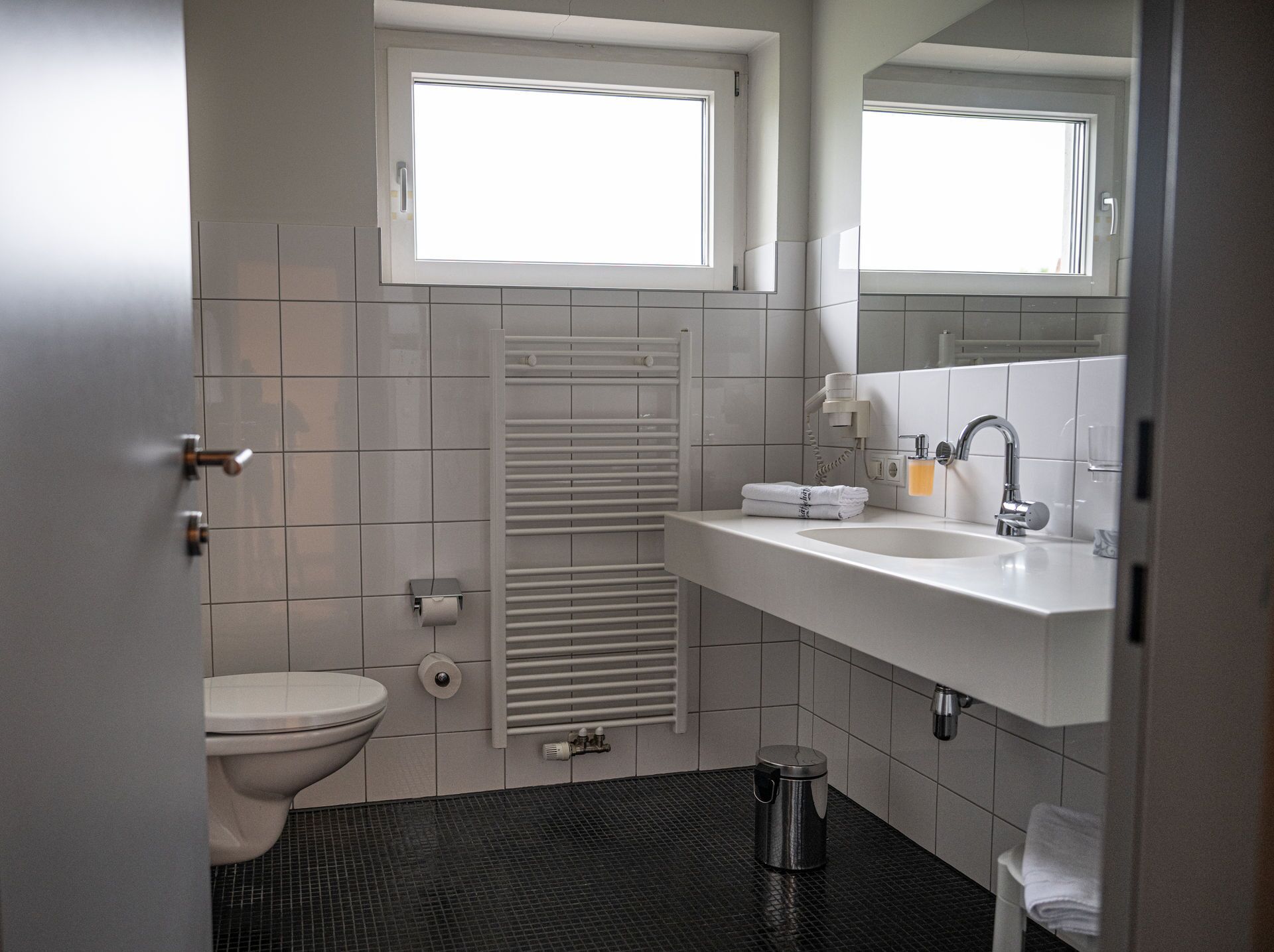 A bathroom with a toilet, sink, towel rack, and a window.