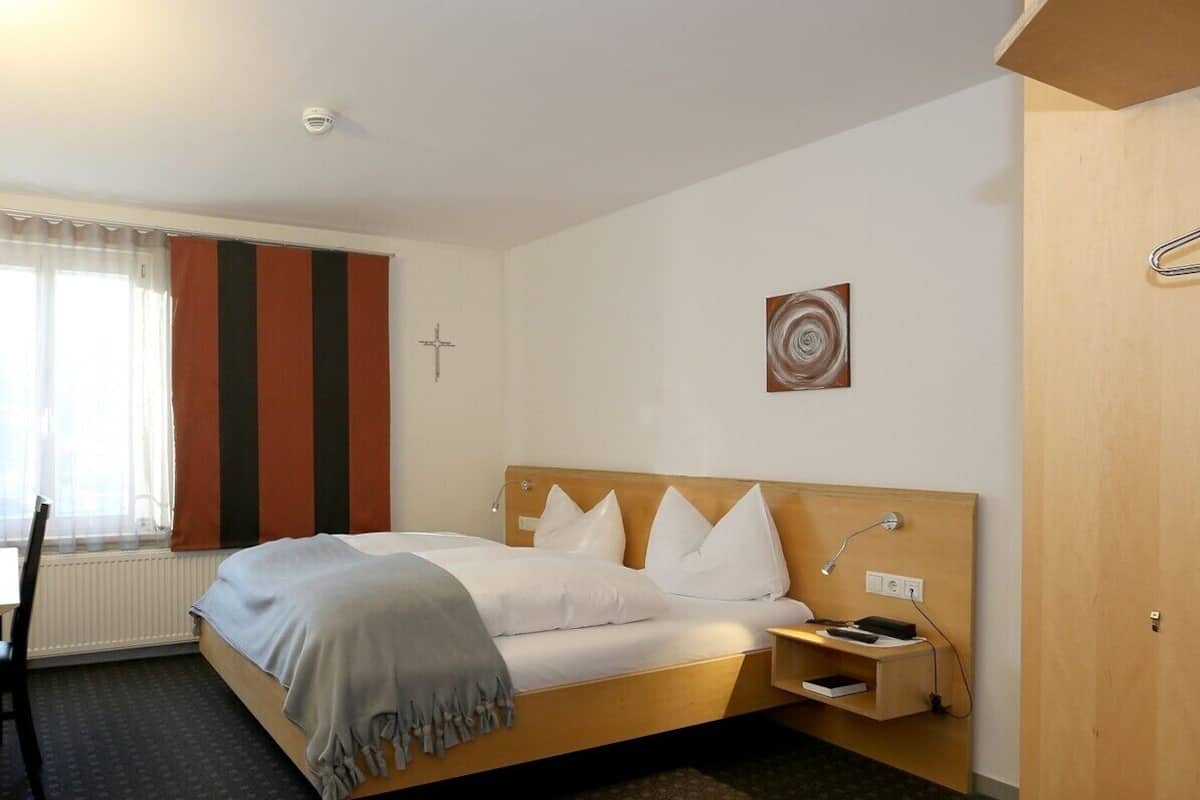 Ein Hotelzimmer mit Bett, Nachttisch, Lampe und einem Fenster mit Vorhängen.