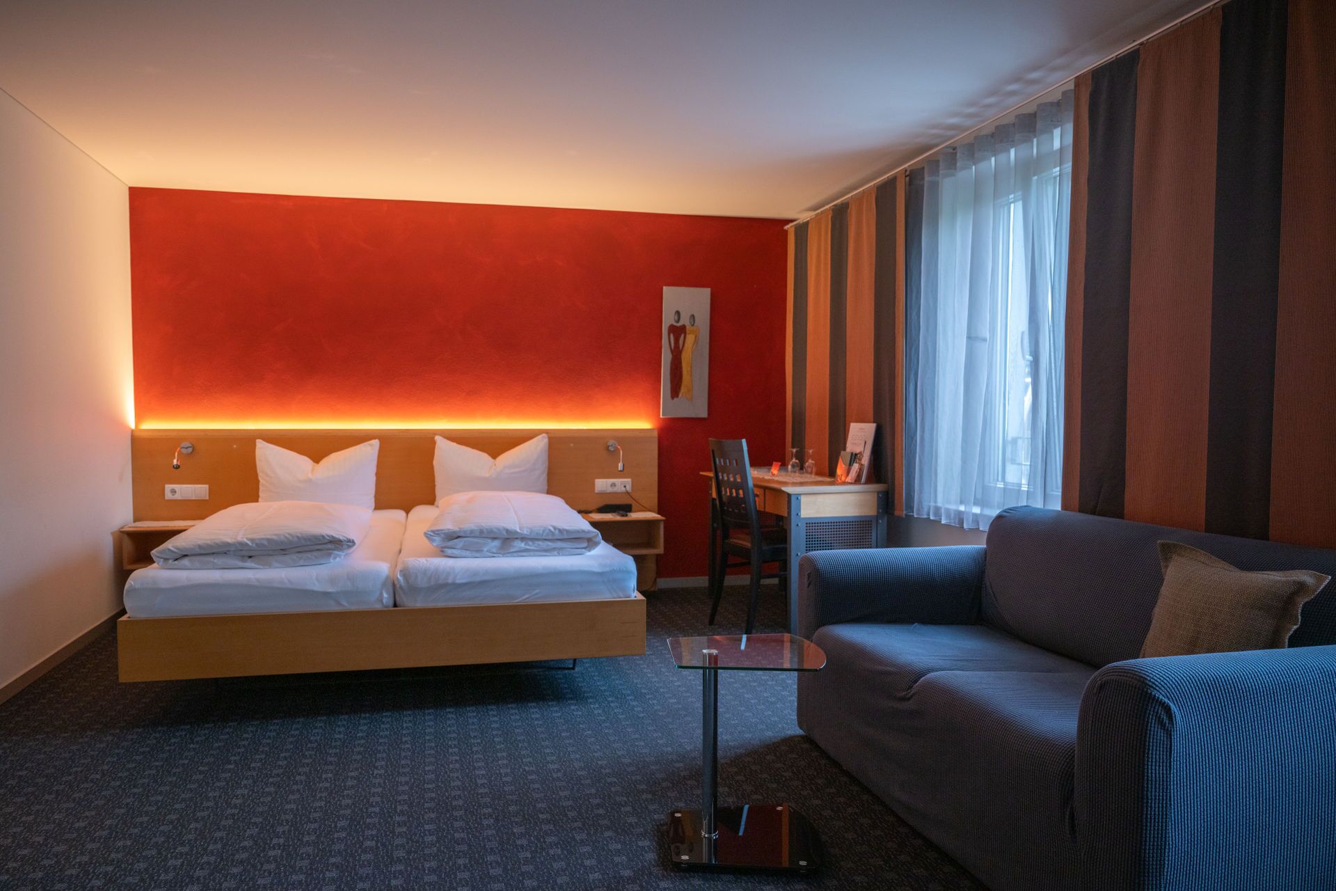 A hotel room with a bed, a desk, a chair, and a sofa.
