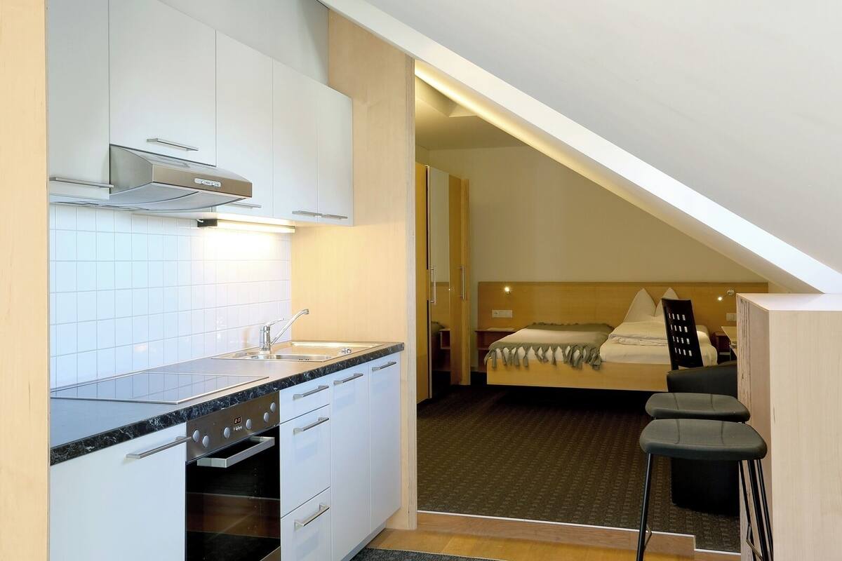 Ein kompaktes Hotelzimmer mit Küchenzeile, einem Bett mit Kopfteil und einer kleinen Sitzecke.