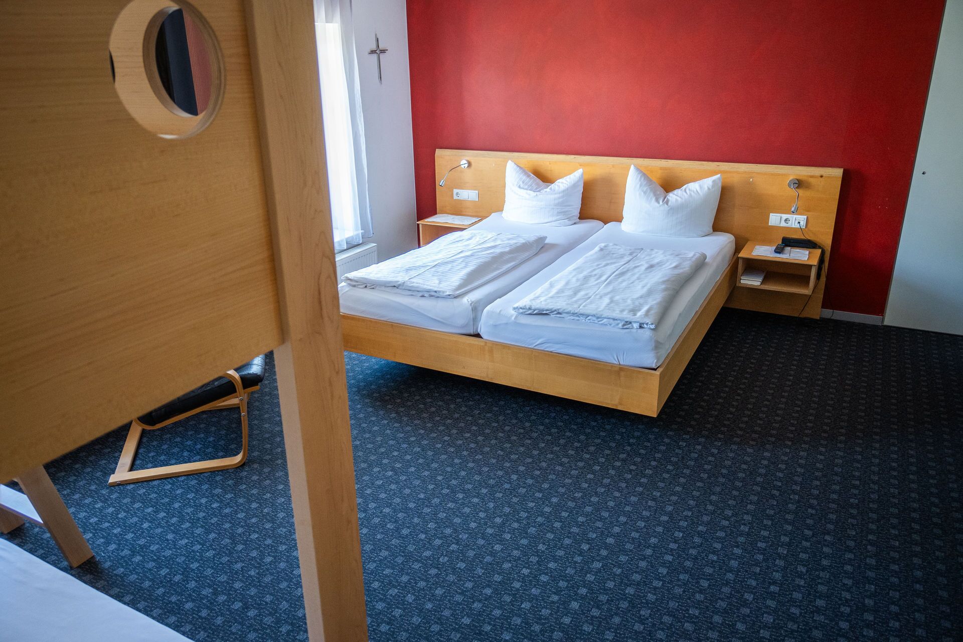 Een tweepersoonsbed met witte lakens, een houten hoofdbord, een nachtkastje met een lamp en een rode accentmuur.