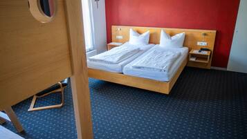 Een tweepersoonsbed met witte lakens, een houten hoofdbord, een nachtkastje met een lamp en een rode accentmuur.