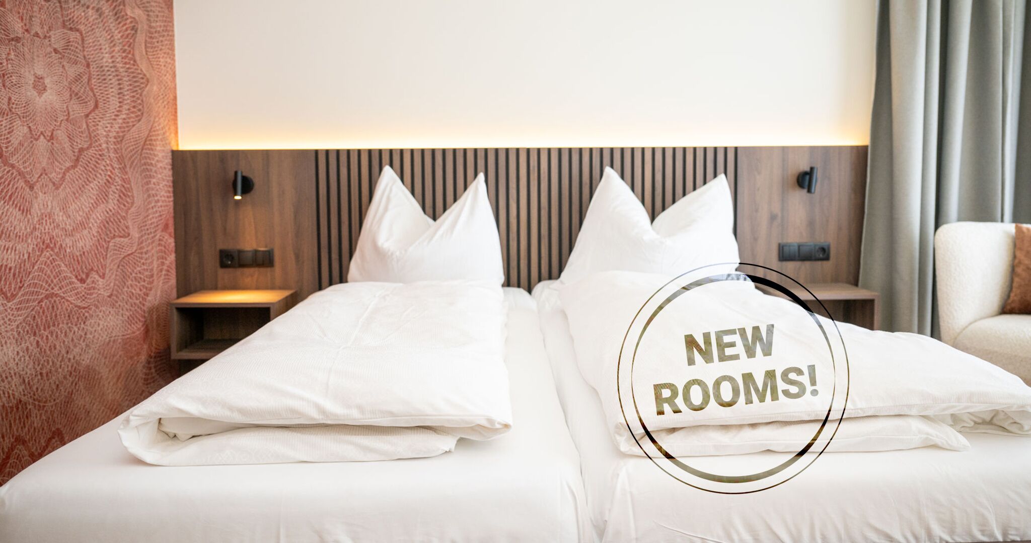 Habitació d'hotel amb dos llits, un capçal de llit de fusta i una tauleta de nit penjada a la paret.
