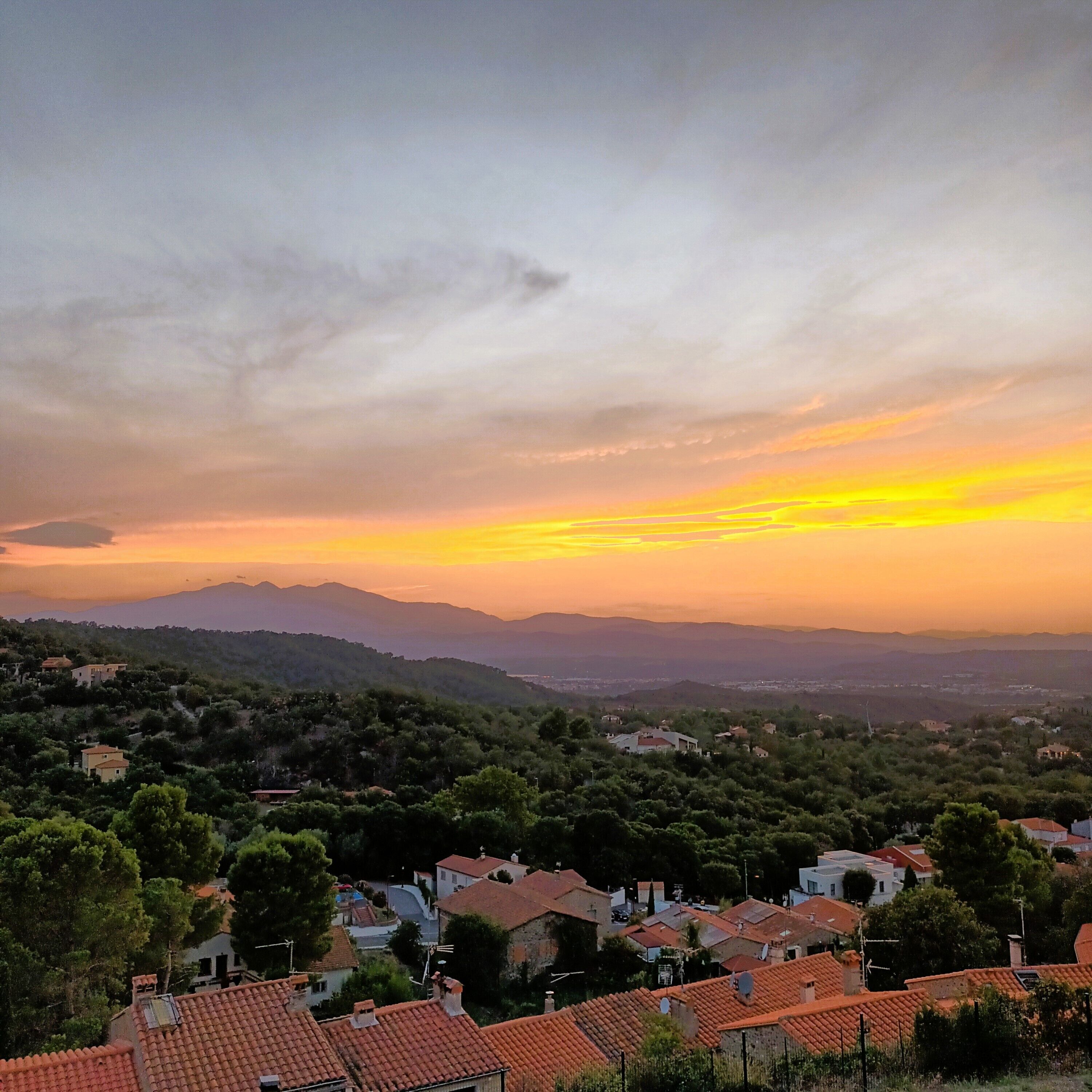 A residential area with houses, trees, and a sunset over the hills.