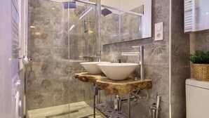 Un baño moderno con cabina de ducha de vidrio, dos lavamanos sobre encimera y una encimera de mármol.