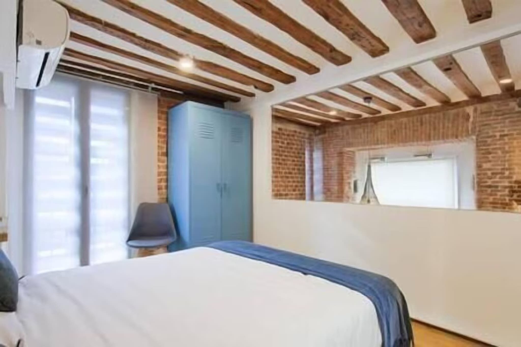 A bedroom with a bed, a wardrobe, and a window with blinds.
