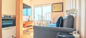 A compact living space with a kitchenette, a sofa, a dining area, and a view of the cityscape.