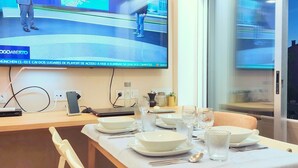 A dining area with a TV displaying a sports channel, a laptop, and a smartphone on a table. - ihW 1-bedroom Apartment Sunny & Comfy (Espinho)