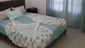 A bedroom with a bed, a nightstand, a wall-mounted air conditioner, and a window with curtains.