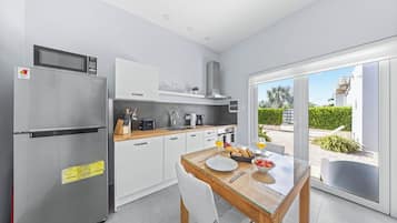 Una cocina moderna con refrigerador de acero inoxidable, armarios blancos y una mesa de madera dispuesta para dos comensales.