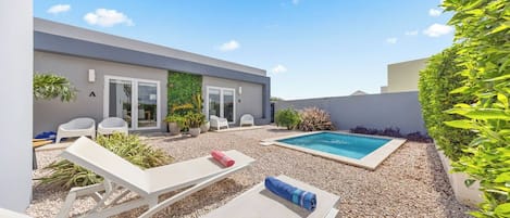A modern outdoor pool area with lounge chairs, a small pool, and a gravel surface.