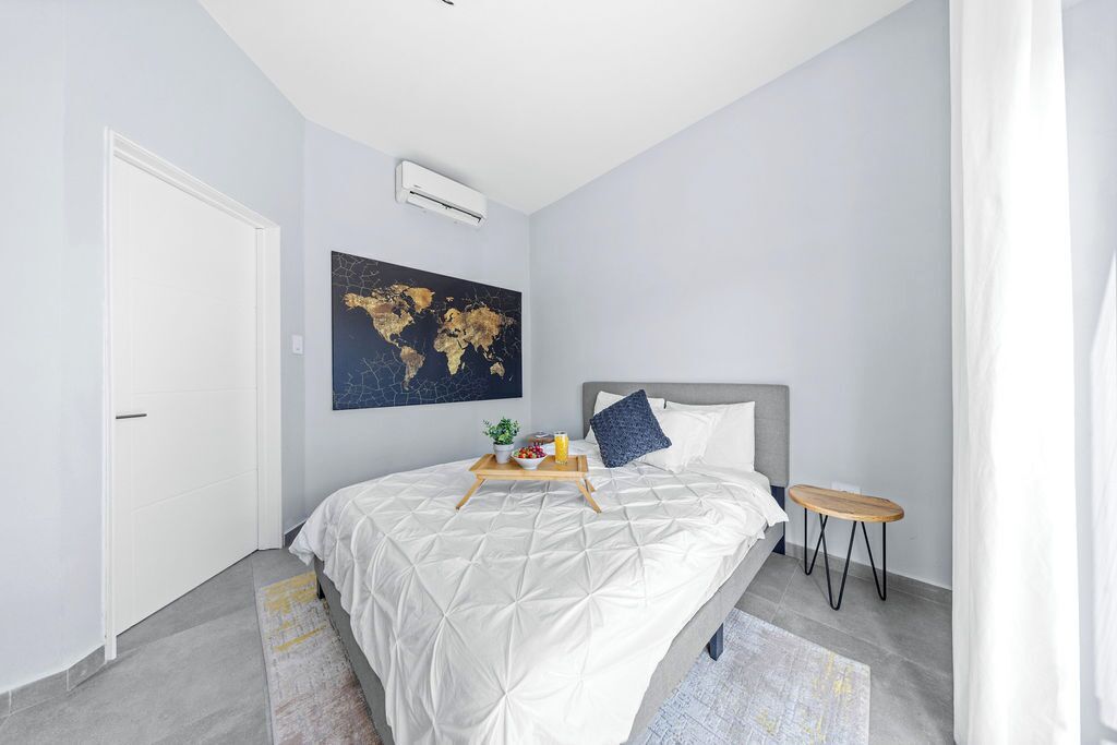Quarto moderno com uma cama, uma mesinha, uma obra de arte com um mapa mundi e uma porta branca.