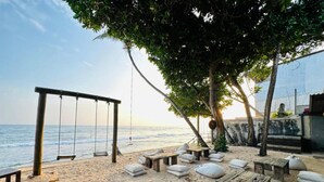 Un cadre idyllique au bord de la plage, avec une balançoire, des tables en bois et des coussins blancs.