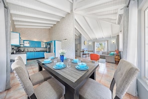 Enjoy meals at the dining table with grey chairs, surrounded by a brick accent wall and high ceiling with exposed beams.
