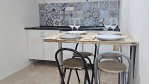 A compact kitchen with a tiled backsplash, a gas stove, and a hanging rack. There are two stools and a table set with plates and glasses. - Cuba Mía  (Burriana)