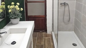 A bathroom with a white sink, a potted plant, a glass shower enclosure, and a wooden door. - Cuba Mía  (Burriana)