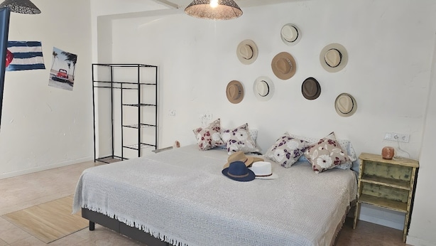 A bedroom with a bed, a hanging light fixture, a wall-mounted hat rack, and a small wooden nightstand. - Cuba Mía  (Burriana)