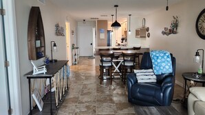A spacious living room with a dark leather sofa, a dining area with a wooden table and chairs, and a kitchen in the background. - Harborfront Views, Rooftop Pool, walking distance to Fishermen's Village! (Punta Gorda)