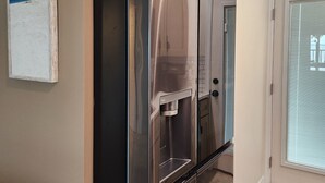 A kitchen with a stainless steel refrigerator, a water dispenser, and a door with a frosted glass panel. - Harborfront Views, Rooftop Pool, walking distance to Fishermen's Village! (Punta Gorda)