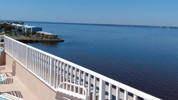 A balcony with a view of the sea, a white railing, and a few lounge chairs. - Harborfront Views, Rooftop Pool, walking distance to Fishermen's Village! (Punta Gorda)