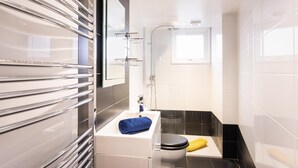 A modern bathroom with a glass shower enclosure, a white sink with a towel, and a black toilet. - Host Stay Ammonite (Lyme Regis)
