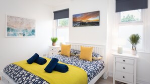 A bedroom with a bed, a bedside table, a window with a view, and a painting on the wall. - Host Stay Ammonite (Lyme Regis)