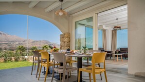 Un coin repas avec une table dressée pour quatre personnes, entouré de chaises jaunes, offrant une vue panoramique sur les montagnes et un vignoble.