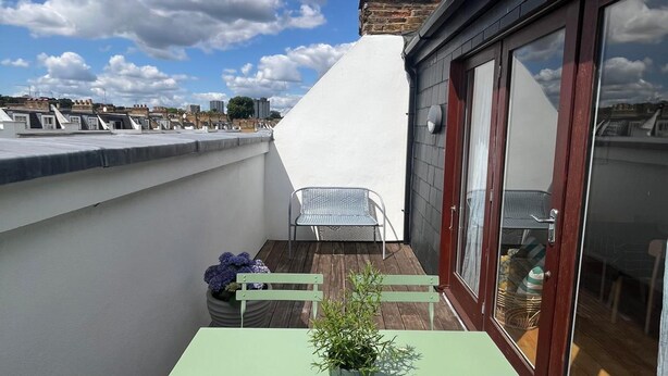 Eine Dachterrasse mit Tisch, Stühlen, einer Topfpflanze und einer Antenne.