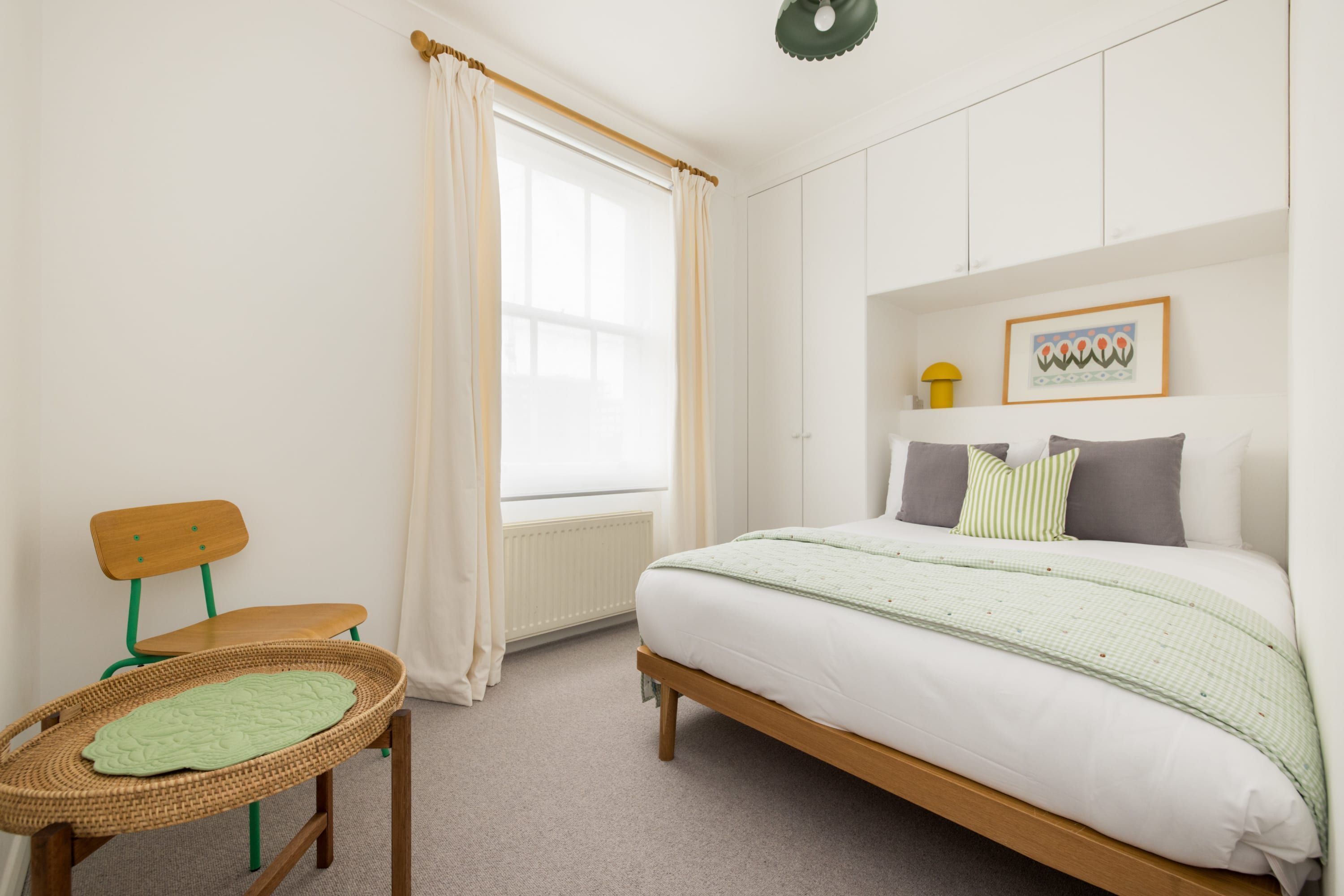 Ein Schlafzimmer mit Bett, Sessel, Fenster mit Vorhängen und Heizkörper.