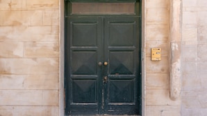 Una puerta doble verde oscuro con un tirador de latón, empotrada en una pared de piedra color beige.