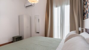 Habitación de hotel con cama, mesita de noche, espejo, equipo de aire acondicionado y ventana con cortinas.