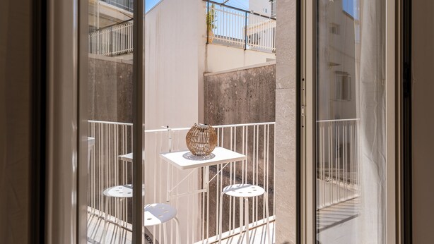Un balcón con mesa y sillas, un jarrón decorativo y vistas a edificios cercanos.