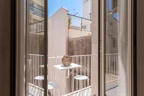 A balcony with a table and chairs, a decorative vase, and a view of adjacent buildings.