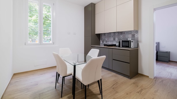 A modern kitchen with white cabinets, a glass dining table, and a view of the outdoors. - Due Agosto Apartment Comfy Modern and Central (Bologna)