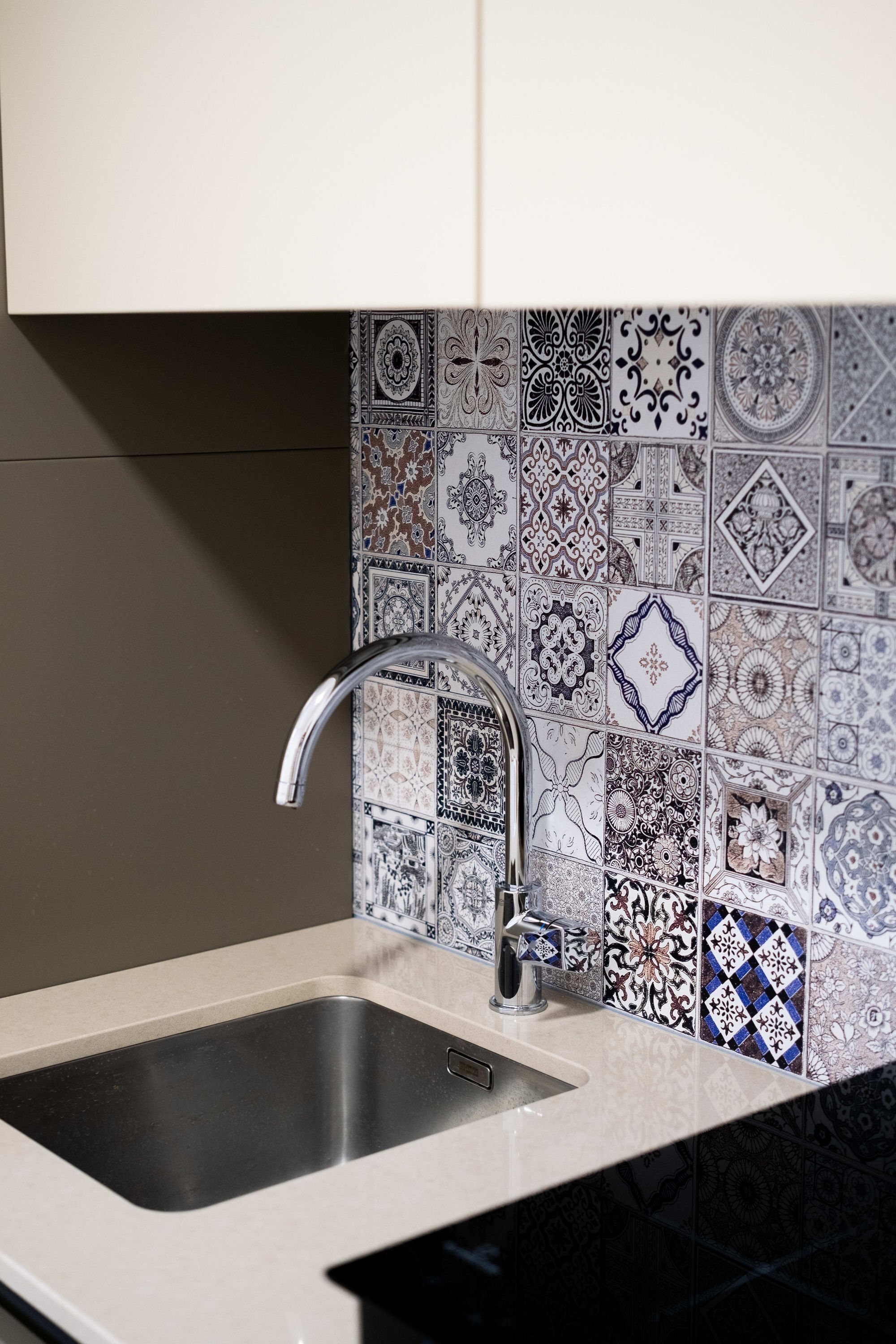 A kitchen with a sink, a faucet, and a backsplash with patterned tiles.