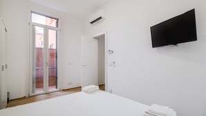 A hotel room with a bed, a flat-screen TV mounted on the wall, a sliding glass door leading to an outdoor area, and an air conditioning unit on the wall. - Due Agosto Apartment Comfy Modern and Central (Bologna)