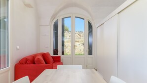 Ein Zimmer mit einem weißen Tisch und Stühlen, einem roten Sofa und einem großen Bogenfenster mit Blick auf felsiges Gelände.