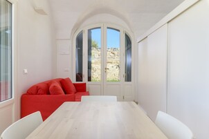 Una habitación con una mesa y sillas blancas, un sofá rojo y un amplio ventanal con vistas a terreno rocoso.