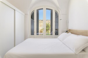 Un dormitorio con cama, paredes blancas, cabecera de madera y vistas a un área exterior a través de un ventanal.