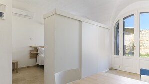 A modern, minimalist room with a wooden table and chairs, a built-in bench, a small bedside table, and a window with a view of rocky terrain.