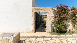 An outdoor seating area with a stone wall, a potted plant, and a clear blue sky.
