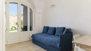 A compact room with a sofa bed, a dining table, and a door leading to an outdoor area.