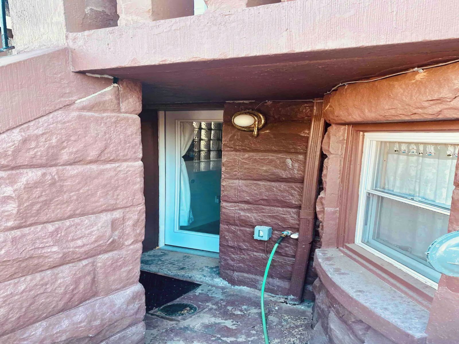 A narrow entrance with a door, a window with a curtain, and a hose connected to an outdoor faucet.