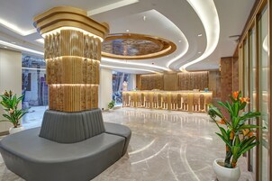 Una hall moderna con un'area salotto centrale, una reception e un soffitto decorato.