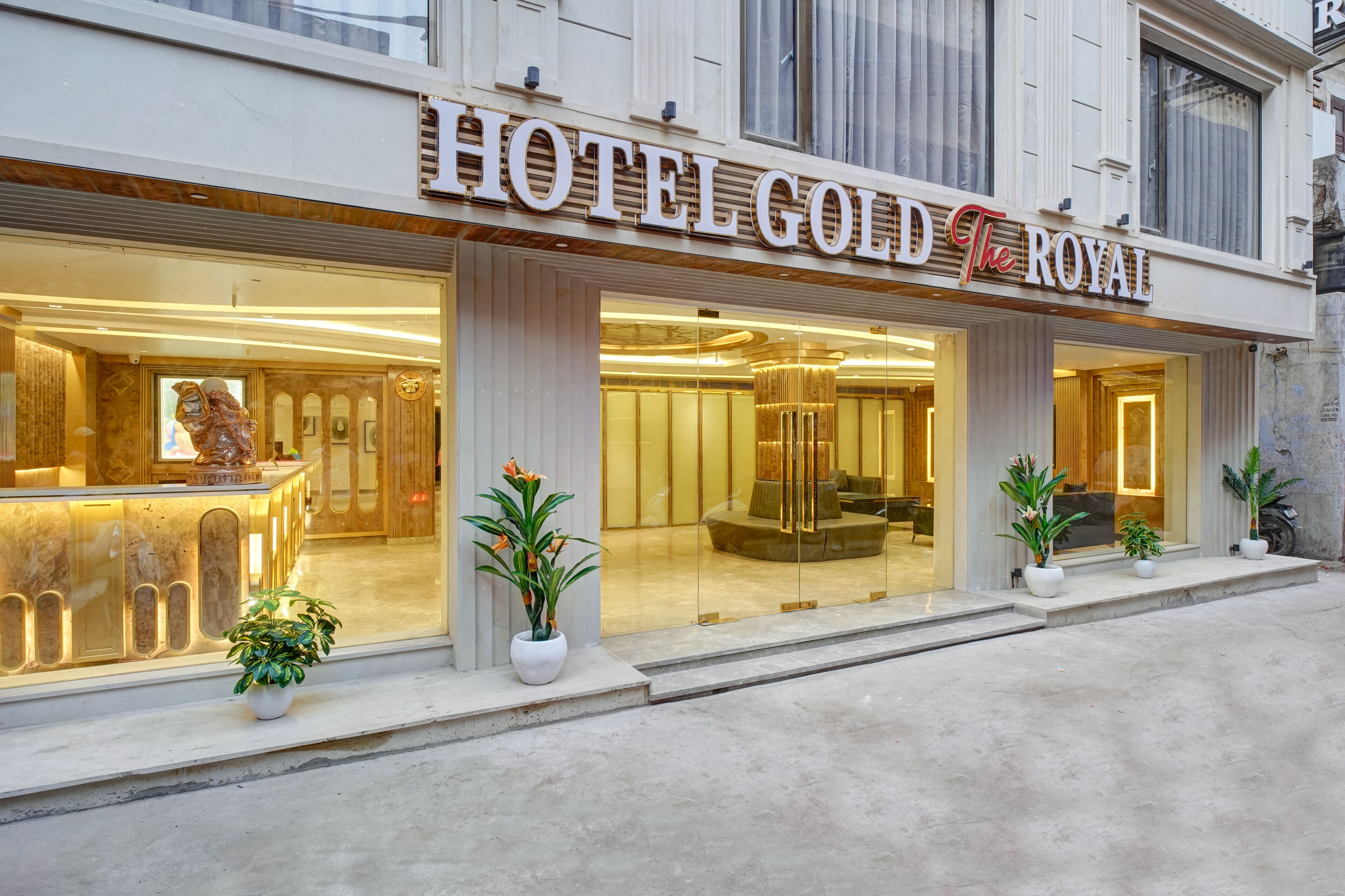 A hotel entrance with a reception desk, potted plants, and a modern interior visible through the glass doors.