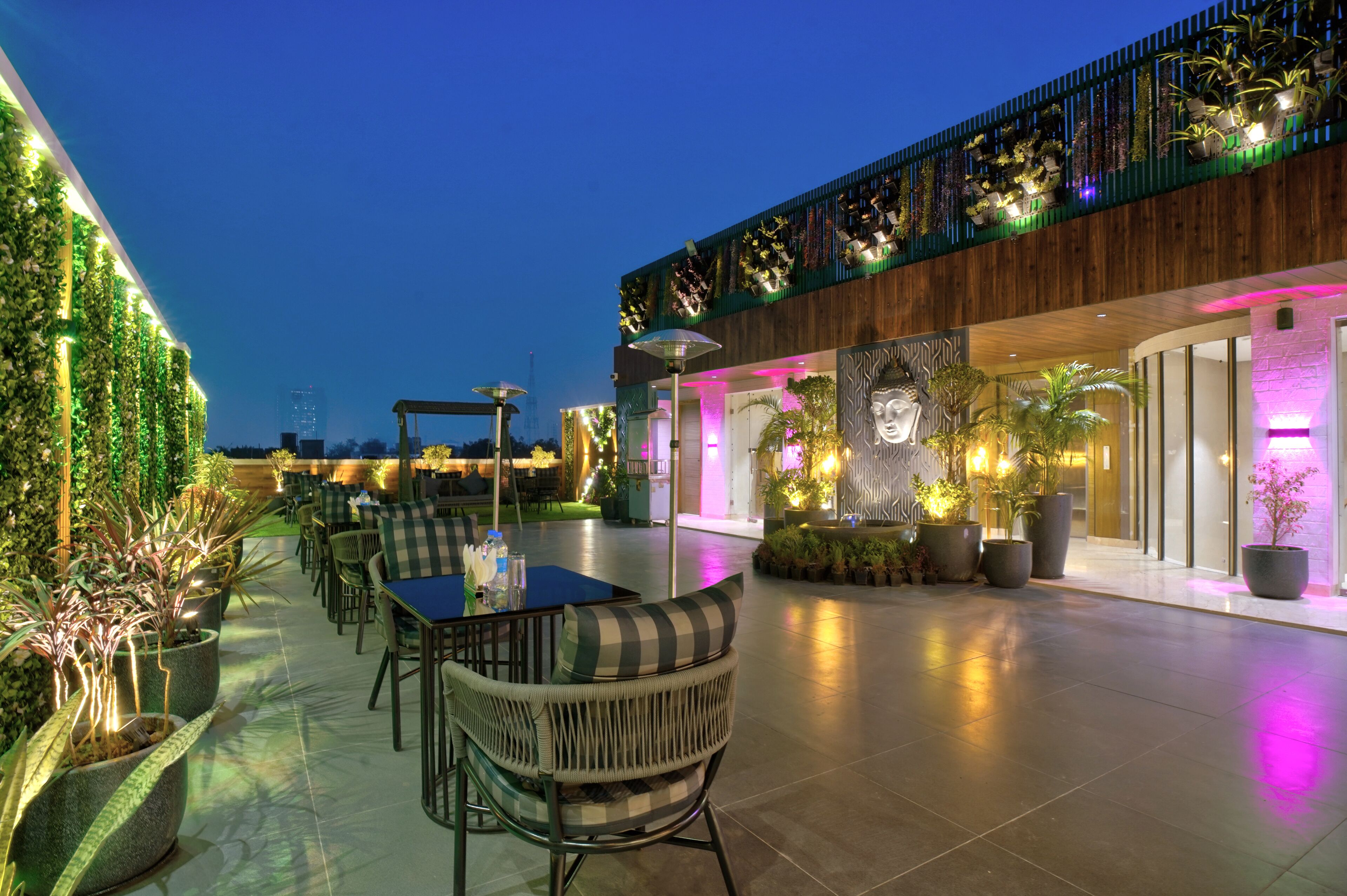 An outdoor dining area with tables and chairs, surrounded by potted plants and a wooden fence.