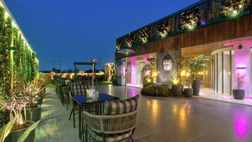An outdoor dining area with tables and chairs, surrounded by potted plants and a wooden fence.