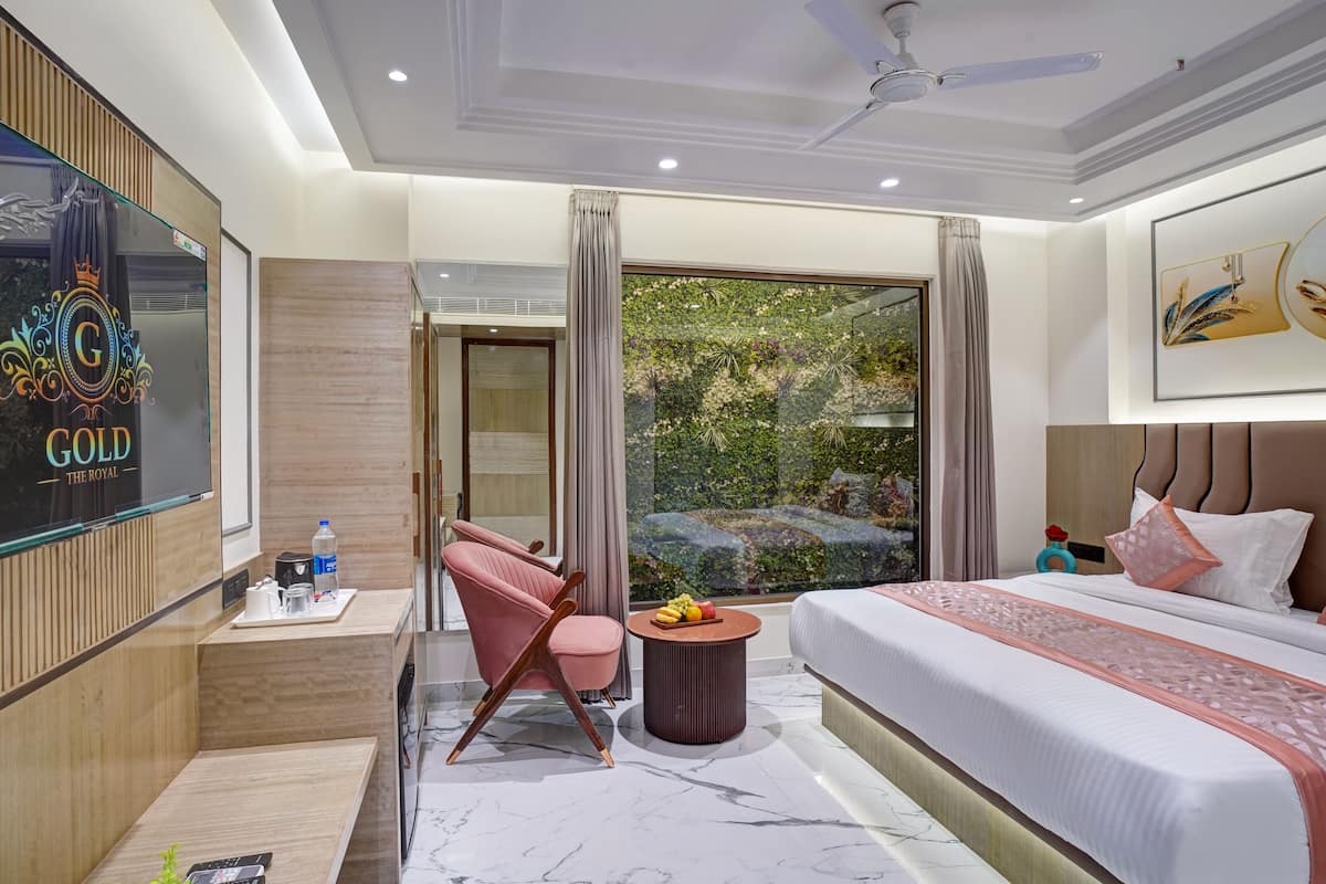 Quarto de hotel moderno com uma cama grande, área de estar com uma cadeira e mesa, televisão e vista para o verde lá fora.