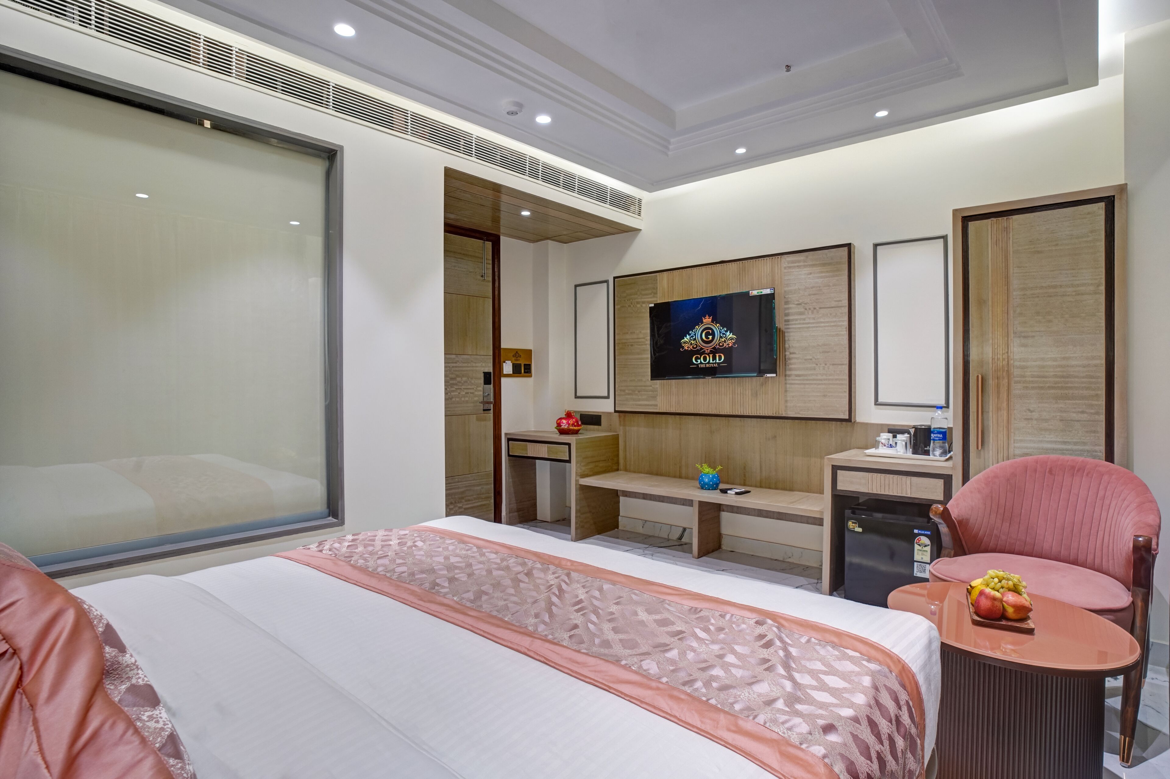 A hotel room with a large bed, a desk, a chair, a TV, and a minibar.